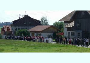 Procesja z okazji święta Bożego Ciała przez ulicę: widać wiernych niosących sztandary, baldachim i księdza